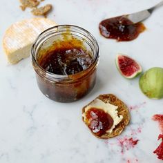 a jar of jam next to sliced figs and crackers on a marble surface