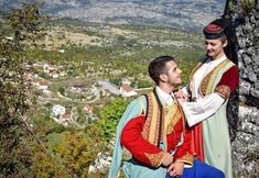 two men dressed in medieval garb standing next to each other on top of a hill