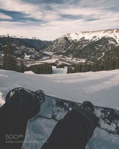 someone is sitting in the snow with their feet propped up and looking at mountains behind them