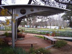 a wooden bench sitting under a metal structure in a park with lots of trees and flowers