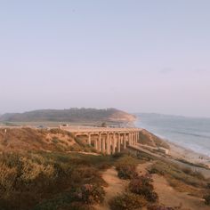 an old train bridge on the side of a hill next to the beach and ocean