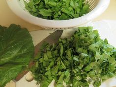 chopped green leafy vegetables on a cutting board next to a strainer and knife