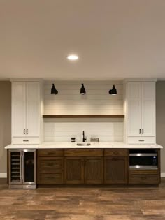 an empty kitchen with white cabinets and wood flooring is pictured in this image, there are three lights on the cabinet above the sink