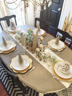 a dining room table set for christmas with gold and white plates, pine cone centerpieces