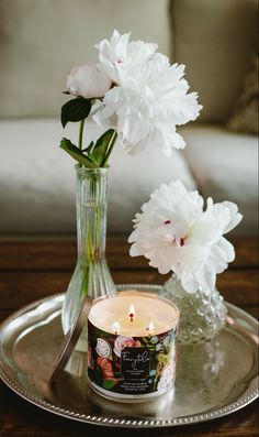 a glass vase filled with white flowers next to a lit candle on top of a metal tray