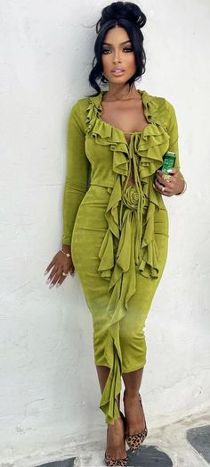 a woman in a green dress leaning against a wall with her hand on her hip