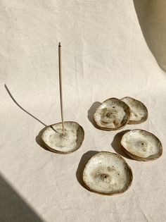 four pieces of pottery sitting on top of a white cloth covered table next to a toothpick