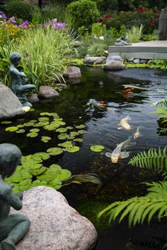 a garden pond with statues and plants surrounding it