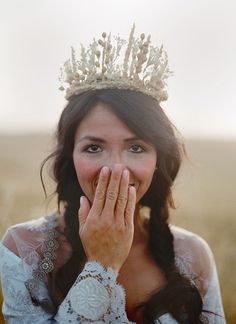 a woman wearing a tiara and holding her hands to her face while standing in a field