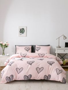 a pink bed with hearts on it in a white room next to a table and flowers