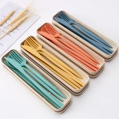 six different colored plastic forks and spoons in a tray with wheat stalks on the side