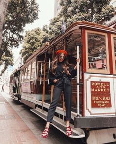 a woman standing on the side of a cable car in front of a tree and building