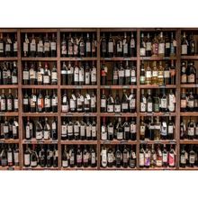 a wall filled with lots of different types of wine bottles on wooden shelves next to each other