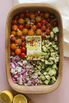 a wooden bowl filled with lots of different types of vegetables next to sliced lemons