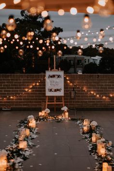 an outdoor wedding ceremony with candles and flowers on the ground in front of a brick wall