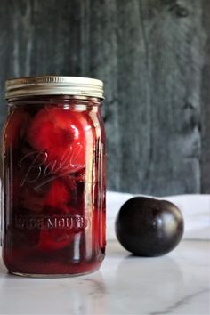 a jar filled with plums sitting on top of a table next to an apple