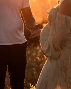 a man and woman holding hands while standing next to each other in front of the sun