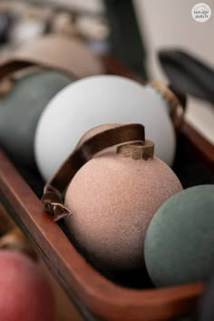 several different colored balls are in a wooden box with a brown ribbon around the edges