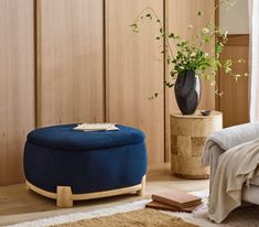 a blue ottoman sitting on top of a wooden floor next to a plant in a vase