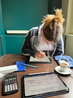 a woman sitting at a table writing on a tablet with a calculator next to her