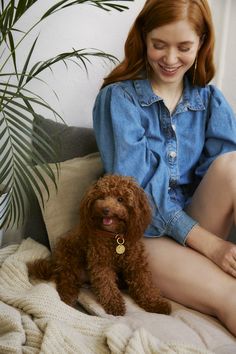 a woman sitting on a couch next to a brown dog and smiling at the camera