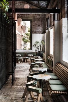 an empty restaurant with wooden benches and plants on the windowsills, in front of a brick wall