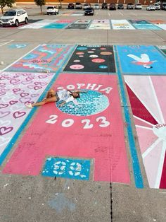 a person laying on the ground in front of a parking lot painted with pink, blue and white designs