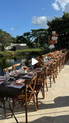 a long table is set up outside by the water for an outdoor party with balloons in the sky