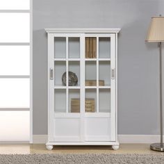 a white bookcase sitting on top of a carpeted floor next to a lamp