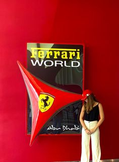 a woman standing in front of a ferrari world sign with her hands on her hips