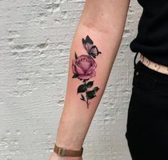 a woman's arm with a pink rose and butterfly tattoo on the left forearm