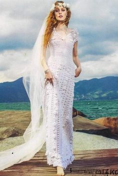 a woman in a white wedding dress standing on a wooden dock near the ocean with her veil blowing in the wind