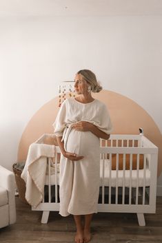 a woman standing in front of a crib with her belly wrapped up and looking at the camera