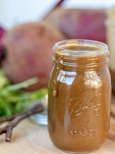 a mason jar filled with brown liquid sitting on top of a table next to vegetables