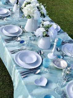 the table is set with blue and white plates, silverware, and flowers in vases