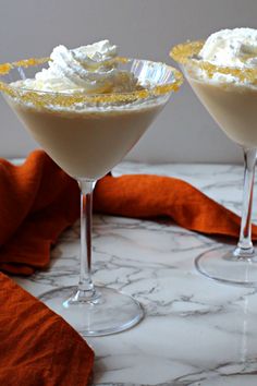 two martinis with whipped cream and orange garnish sit on a marble table