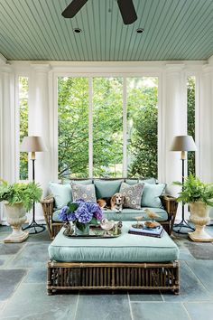 a living room filled with lots of furniture next to a large window and ceiling fan