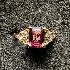 a pink and white diamond ring sitting on top of a black surface with gold accents