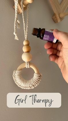 a hand holding an essential oil bottle in front of a wooden bead hanging from the ceiling