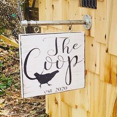 a sign that says the coop hanging on a wooden fence post in front of a chicken coop