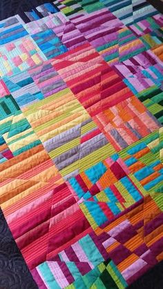 a colorful quilt is laying on top of a black table cloth and it's made from strips of multicolored fabric