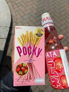 a person holding up a box of popsy strawberries and a bottle of soda