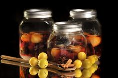 three glass jars filled with different types of fruit and spices sitting on a wooden table