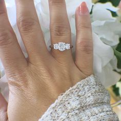 a woman's hand with a diamond ring on it and flowers in the background