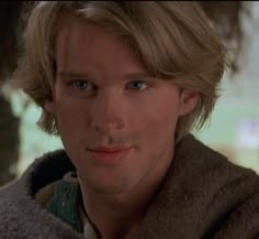 a young man with blonde hair and blue eyes looks into the camera while wearing a sweater