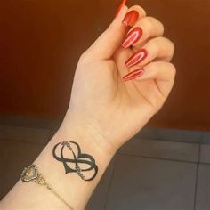 a woman's hand with red nail polish holding up a small tattoo on her wrist