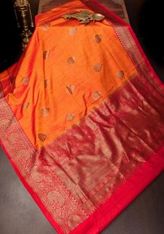 Dupion Silk is a unique kind of silk known for its matt texture. The use of antique gold tone zari gives it a regal look. The saree is sought after for its rustic charm and never fails to make a statement.  This pure Dupion Silk Saree comes in a combination of mustard and orange stripes wirh red borders. It features antique zari damask zari buttas and beldar vine borders.  SILK MARK CERTIFIED This saree is ready to wear with fall and pico done. Handmade silk tassels adorn the pallu and add more