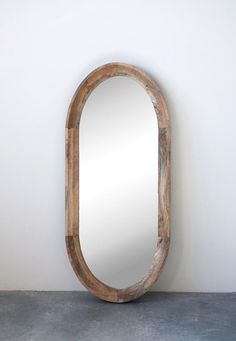 an oval wooden mirror sitting on top of a cement floor next to a white wall