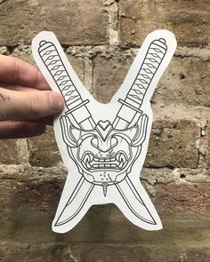 a hand holding up a sticker with a demon face on the front and two swords in