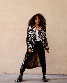 a woman standing in front of a wall wearing a long coat and black pants with an animal print design on it